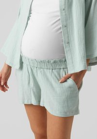 Světlé zelené, texturované bavlněné šortky s elastickým pasem a kapsami, nošené s odpovídajícími oversized košilí na knoflíky.