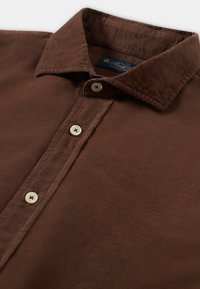 Bruine corduroy shirt met een button-down kraag, vijf knopen en een subtiele textuur. Heeft een marineblauwe label aan de binnenkant van de kraag.