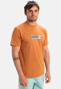 Camiseta de algodón naranja con un diseño rectangular del logo de Quiksilver en la parte frontal, mangas cortas y un clásico cuello redondo.