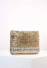 Kultainen paljettikukkaro, jossa on hopean- ja mustanväriset vaakaraitat, varustettu ketjunauhoilla ja sivulla oleva pyöreä logokiinnitys.