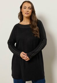 Haut en tricot noir à manches longues, avec des accents à œillets le long des épaules. Coupe ample, encolure ronde et texture douce.