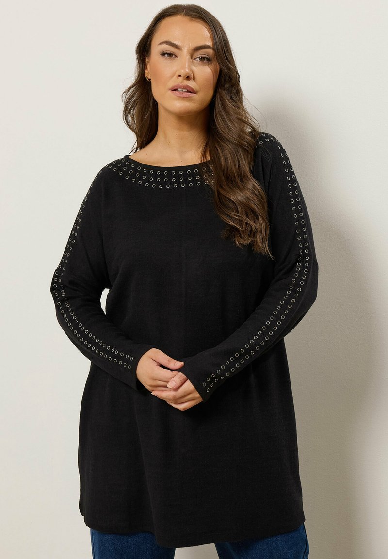 Haut en tricot noir à manches longues, avec des accents à œillets le long des épaules. Coupe ample, encolure ronde et texture douce.