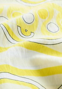 Tissu avec des formes abstraites jaunes et blanches bordées de noir, comprenant des cercles et des lignes courbes sur un tissu doux et drapé.