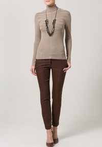 Beige ribbestrikken turtleneck genser med vertikale striper, parret med tettsittende brune mønstrede bukser med heksagonal design og høye hæler.