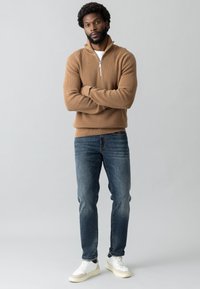 Pruun ribadega neljandikruvi särk, valge T-särk all, sinised denimii teksad ja valged sneekerid mustade aktsentidega. Lihtne, modernne disain.