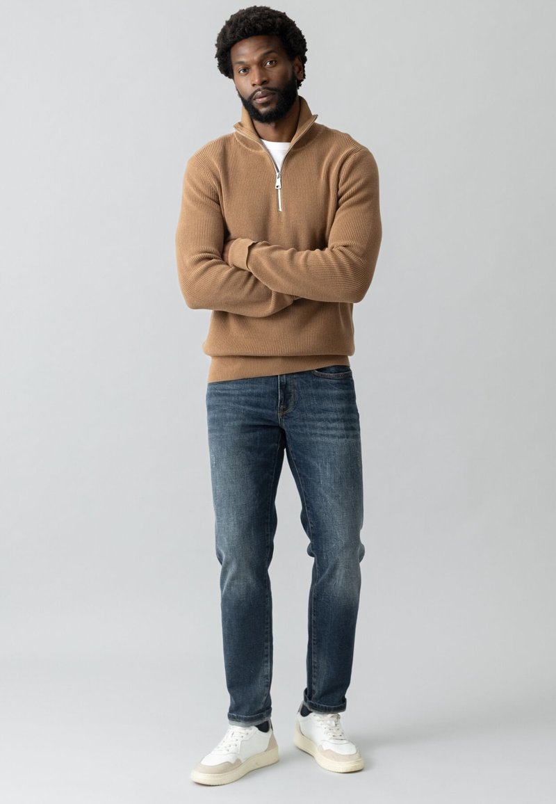 Pruun ribadega neljandikruvi särk, valge T-särk all, sinised denimii teksad ja valged sneekerid mustade aktsentidega. Lihtne, modernne disain.