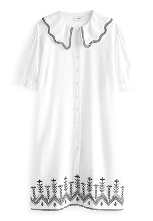 Robe blanche avec un col rond orné de bordure noire. Manches courtes bouffantes et devant à boutons. Broderie florale noire à l'ourlet.