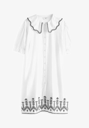 Robe blanche avec un col rond orné de bordure noire. Manches courtes bouffantes et devant à boutons. Broderie florale noire à l'ourlet.