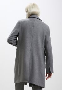 Cappotto grigio di lana con colletto a rever, maniche lunghe e taglio dritto. Presenta una finitura testurizzata e tasche laterali nascoste.