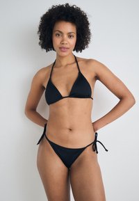 Crni bikini set s trokutastim grudnjakom i podesivim donjim dijelom na vezanje sa strane. Napravljen je od glatkog materijala s minimalnim ukrasima.