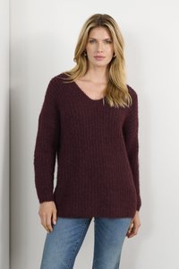 Burgunderfarbener Strickpullover mit V-Ausschnitt, strukturiertem Oberflächen und langen Ärmeln. Kombiniert mit blauen Jeans im lässigen Schnitt.