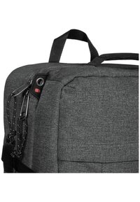 Šedý látkový batoh se strukturovaným designem, vybavený horním držákem, zipy, kovovými akcenty a texturovaným povrchem.