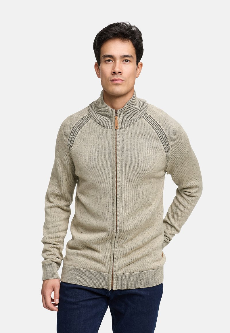 Beige ritssluiting trui met een hoge kraag, geribde textuur en contrasterende bruine rits. Heeft raglanmouwen en een aansluitende taille.