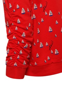 Rode sweatshirt met een geribbelde textuur, voorzien van een patroon van kleine zeilboten in blauw, wit en rood, en de tekst "Ahoy!" in zwart.