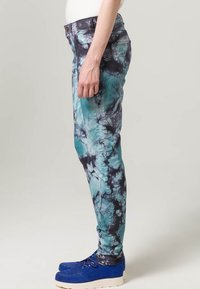 Jean skinny tie-dye en teal et noir, avec bouton et poches avant. Portés avec des chaussures en daim bleu.