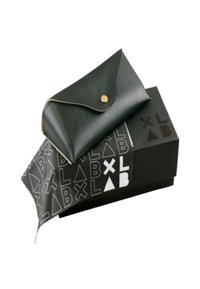 Svart läderfodral med en böjd klaffstängning och guldknopp, vilande på en svart låda med ett vitt geometriskt mönster. Inkluderar en rengöringsduk.