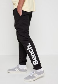 Pantalons de survêtement noirs au design sportif, avec un grand logo "Bench." blanc sur la jambe gauche, en tissu doux et avec une coupe fuselée.