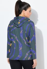 Kapuzenshirt mit langen Ärmeln in Dunkelgrün mit einem welligen, lila und gelben abstrakten Muster. Glatter Stoff mit einer lässigen Passform.