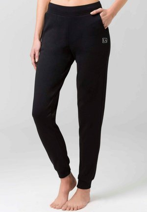Schwarze Jogginghosen mit schmalem Schnitt, elastischem Bund, seitlichen Taschen und dezentem Logodetail. Hergestellt aus weichem Stoff mit glatter Textur.