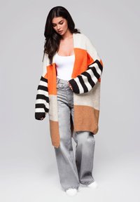 Sweter z dzianiny w pomarańczowe, beżowe oraz czarno-białe paski. Luźny krój z szerokimi rękawami, zestawiony z jeansami o wysokim stanie.