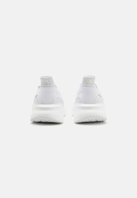 Zapatillas deportivas blancas con un upper de textil suave, suela acolchada y un sutil logotipo en el talón y la parte trasera. Diseño ligero.
