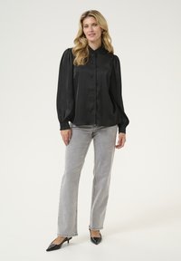 Blusa nera in satin a maniche lunghe con chiusura a bottoni e colletto arricciato, abbinata a jeans grigi chiari a gamba dritta e décolleté neri a punta.