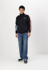 Ναυτική αθλητική ζακέτα με φερμουάρ σε ναυτικό χρώμα με κόκκινες και λευκές ρίγες, συνδυασμένη με ανοιχτό μπλε τζιν και ναυτικά sneakers. Αξεσουάρ: μικρή ανοιχτό μπλε τσάντα.