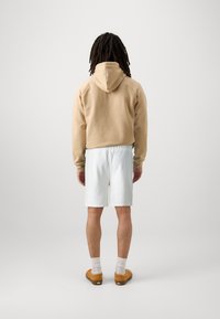 Sudadera corta beige, pantalones cortos blancos y zapatos marrones. La sudadera cuenta con capucha y puños acanalados; los pantalones cortos tienen una cintura elástica.