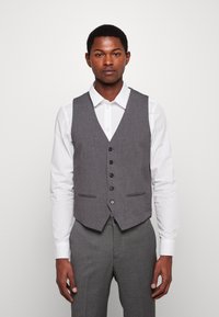 Hall gray villane vest, mille on nelinurkne krae, viis musta nuppu ning kaks esipocketit, koos valge kaelusega särgiga.