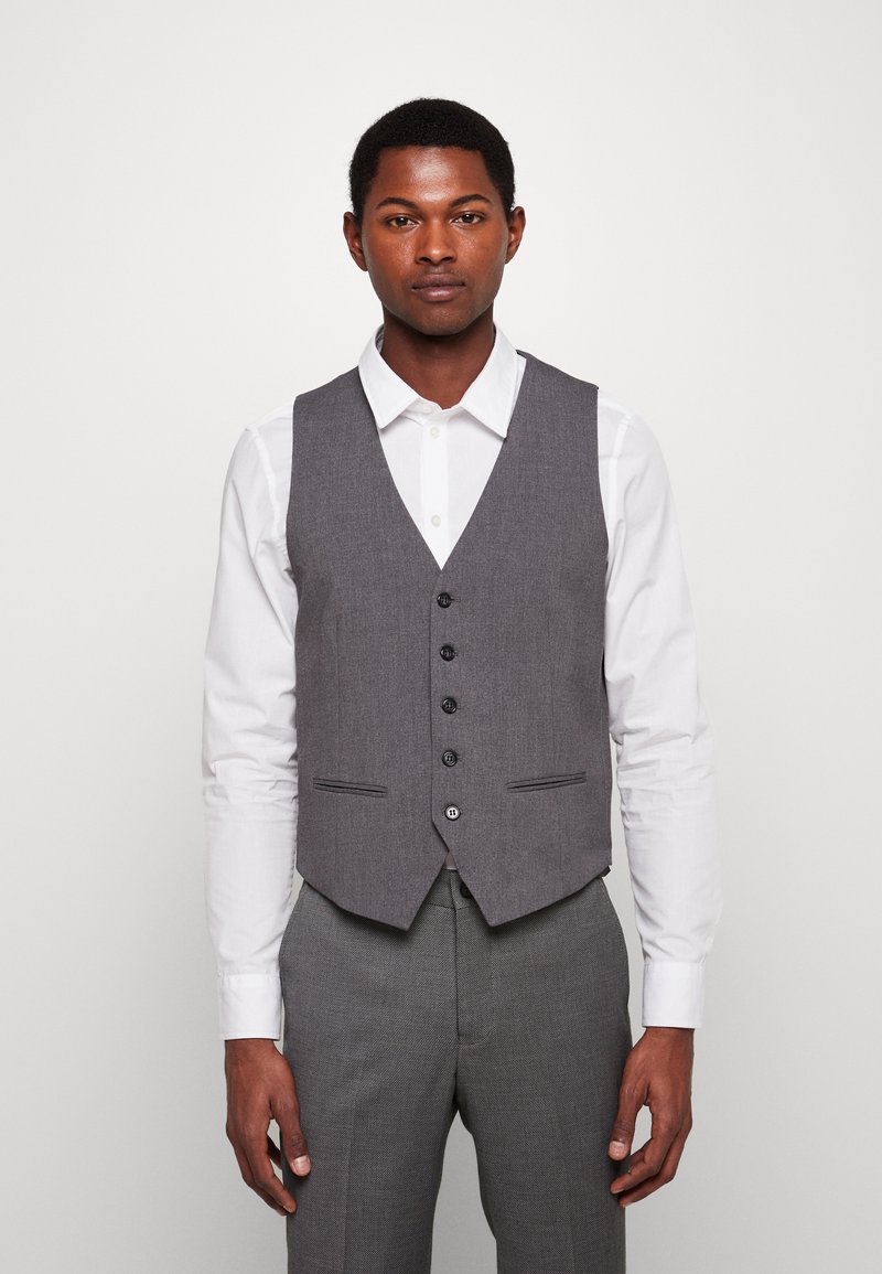 Hall gray villane vest, mille on nelinurkne krae, viis musta nuppu ning kaks esipocketit, koos valge kaelusega särgiga.