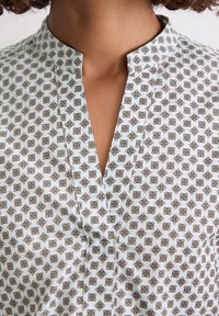 Chemise à manches longues avec un fond blanc ornée d'un motif géométrique en marine, or et bleu clair. Col cranté avec des coutures discrètes.