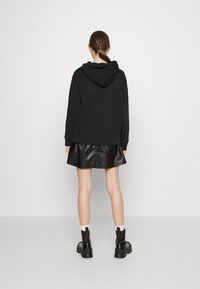 Sudadera negra con capucha y bolsillo canguro, combinada con una minifalda de cuero negra y botines negros. Textura lisa, diseño casual.