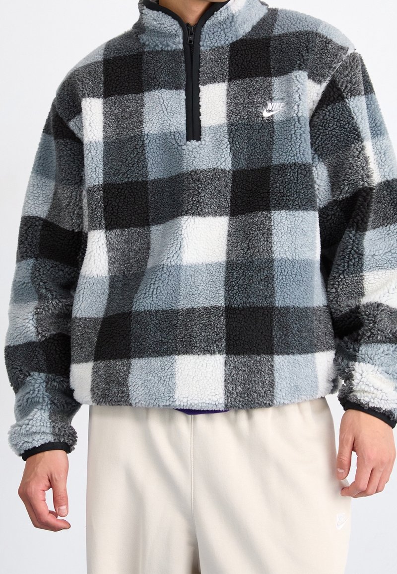 Fleece-pullover i svart, grå och ljusblå rutmönster. Har en fjärdedelsdragkedja och en Nike-logotyp på övre vänstra bröstet.