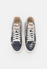 Höga sneakers i slitstark blå denim med vita detaljer, utrustade med vita skosnören och en logotypetikett på tungan. Flat gummisula.