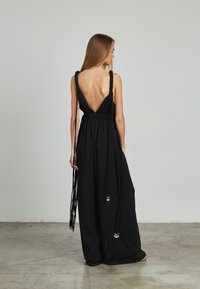 Vestido maxi negro con la espalda al descubierto y tirantes gruesos, con acentos trenzados y tejido texturizado. Largo hasta el suelo y de corte holgado.