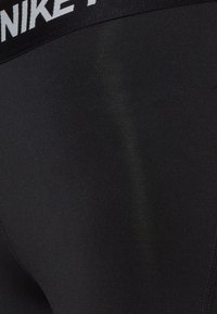 Czarne elastyczne legginsy z szerokim paskiem w talii, na którym znajduje się biały logo Nike. Gładka tekstura i dopasowany krój.