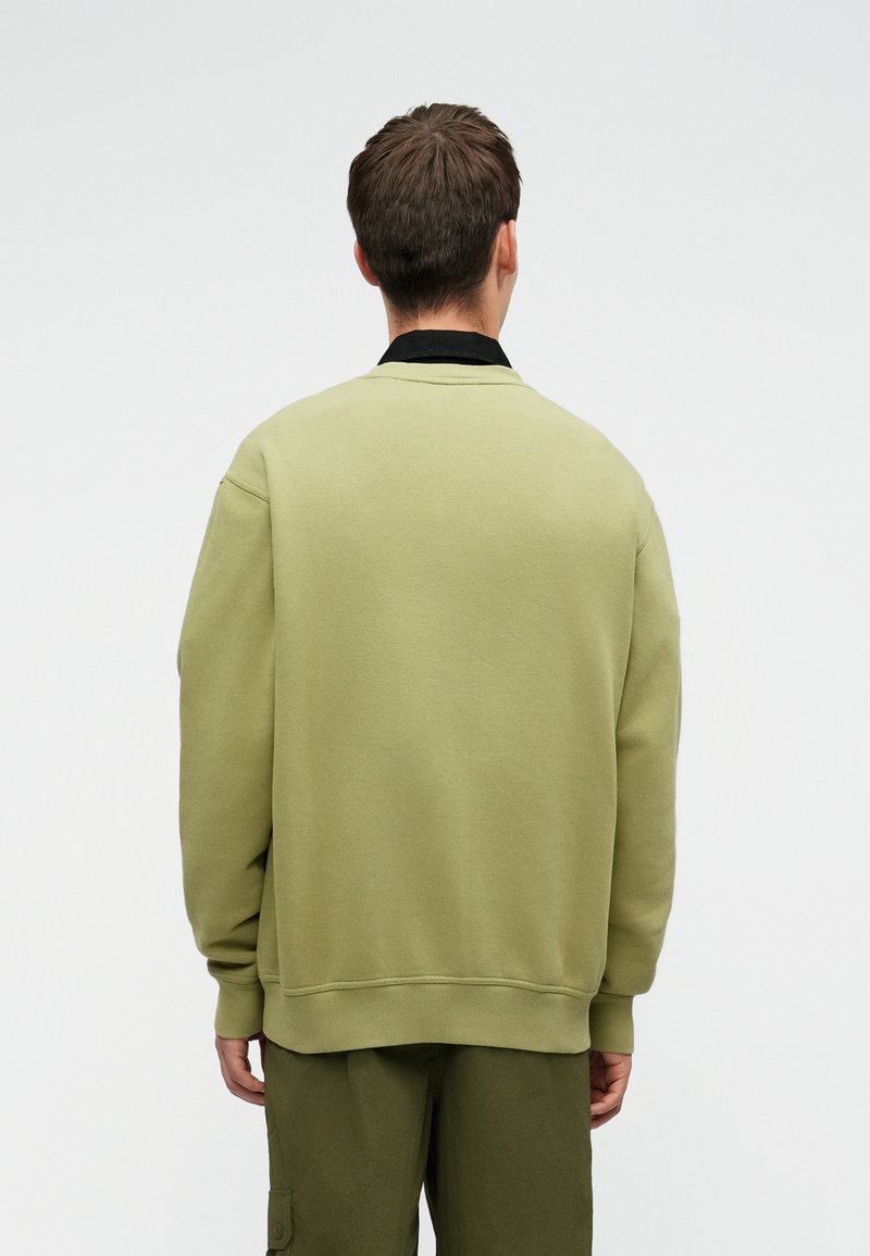 Sudadera de cuello redondo de gran tamaño en verde oliva claro, con puños y dobladillo acanalados, que presenta un cuello negro superpuesto por debajo.