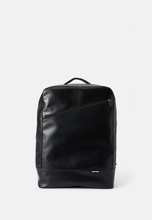 Sac à dos noir en matériau lisse et mat, équipé d'une poche zippée à l'avant, d'une poignée supérieure et d'un design minimaliste.
