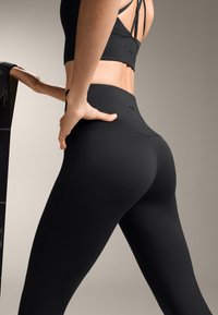 Čierne legíny a zodpovedajúci športový podprsenka vyrobené z hladkej, elastickej látky. Legíny majú vysoký pás a elegantný dizajn bez viditeľných log.