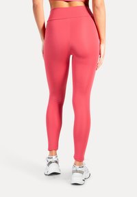 Roze legging gemaakt van elastische stof, met een hoge tailleband, een slanke pasvorm en een gladde textuur. Gecombineerd met witte sneakers.