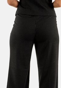 Pantalones de rayas negras hechos de un material suave, con una cintura alta y un diseño de pierna ancha. Las rayas verticales con un ligero brillo añaden detalle.