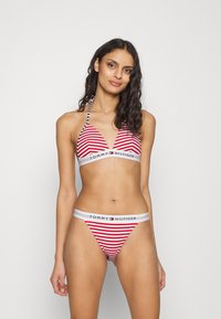 Röd och vit randig bikini med triangulär topp och logoband; halterneck med svart och vit randiga knytband; minimal täckning underdel.