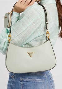 Jasnozielona torebka o teksturowej powierzchni, z złotym trójkątnym logo, złotymi akcentami i odpinaną mini saszetką na pasku.