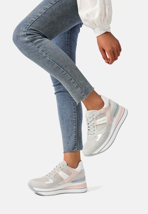 Sneaker grigio chiaro con accenti rosa e dettagli bianchi, caratterizzati da una tomaia testurizzata e una suola bianca spessa, indossati con jeans skinny blu.