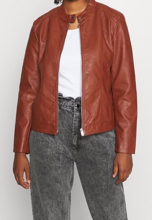 Braune Lederjacke mit Stehkragen, Frontreißverschluss und seitlichen Nähten. Kombiniert mit hochgeschnittenen, verschlissenen grauen Jeans.