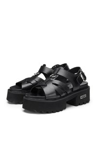 Sandali neri con piattaforma e cinghie incrociate, realizzati in materiale sintetico liscio, con suola spessa e accenti in metallo argentato.