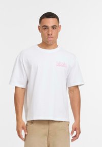 Camiseta de algodón blanca de mangas cortas, con un estampado gráfico rosa en el lado izquierdo del pecho. Textura lisa, corte relajado.