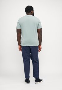 Ανοιχτό πράσινο κοντομάνικο μπλουζάκι, μείγμα από βαμβάκι, με στρογγυλή λαιμόκοψη, σε συνδυασμό με ναυτικό παντελόνι, εκτεθειμένο από πίσω, που δείχνει τη συνολική εφαρμογή και τη σιλουέτα.