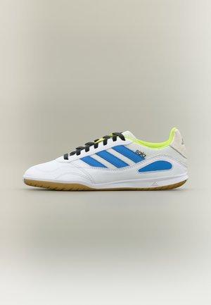 Scarpa da ginnastica bianca con accenti blu e neri, pelle testurizzata, suola in gomma e colletto imbottito. Presenta un design con tre strisce.