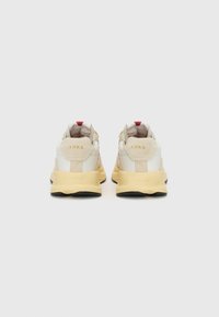 Cream and tan athletic shoes with a padded collar and red accents. Features a low profile and a rubber black sole with brand logo details.